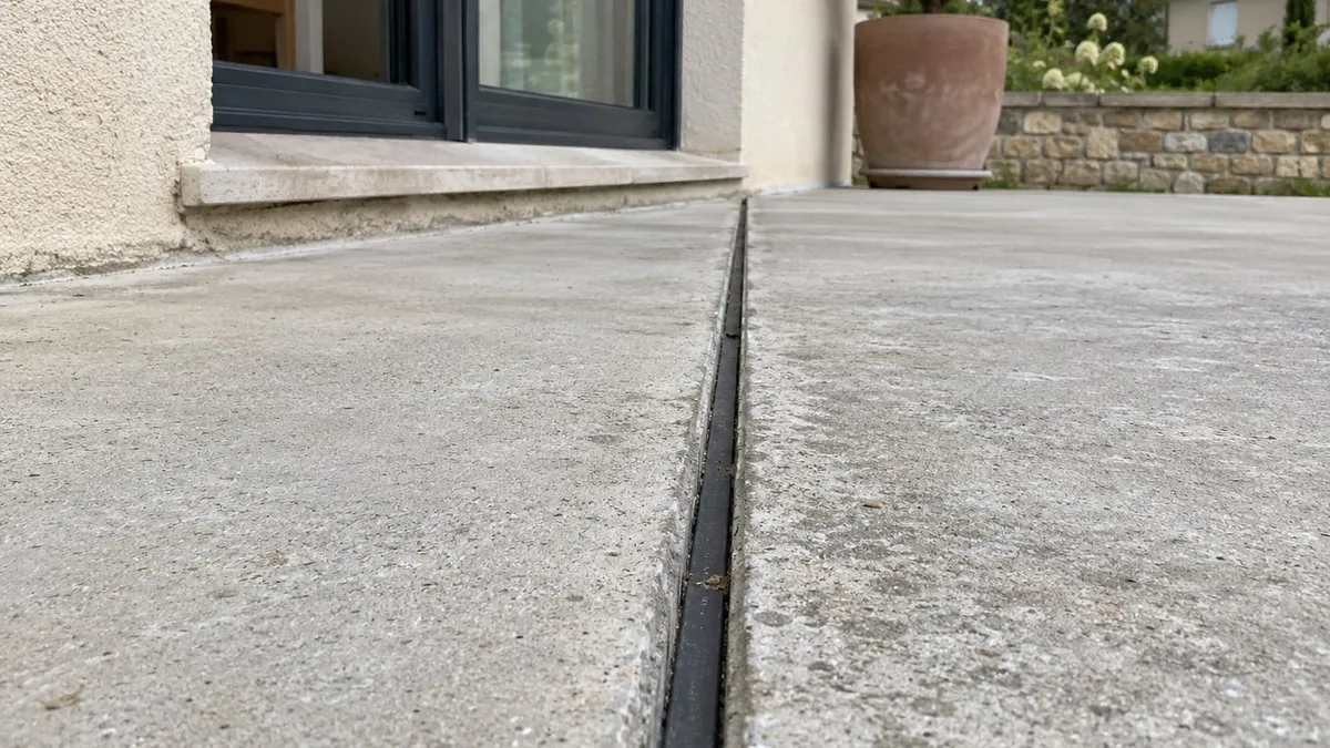 Dalle béton extérieure avec joint de dilatation souple et propre, fissures fines visibles en arrière-plan