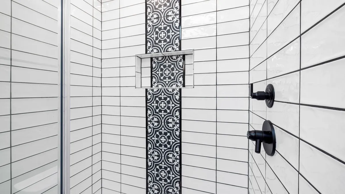 Salle de bain moderne aux murs carrelés en faïence grise, baignoire blanche et miroir rond